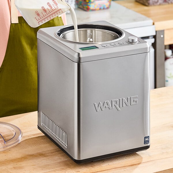 A person pouring milk into a silver Waring ice cream machine.