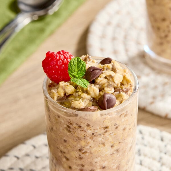 A glass filled with overnight oats topped with chocolate chips, a raspberry, and a mint leaf.