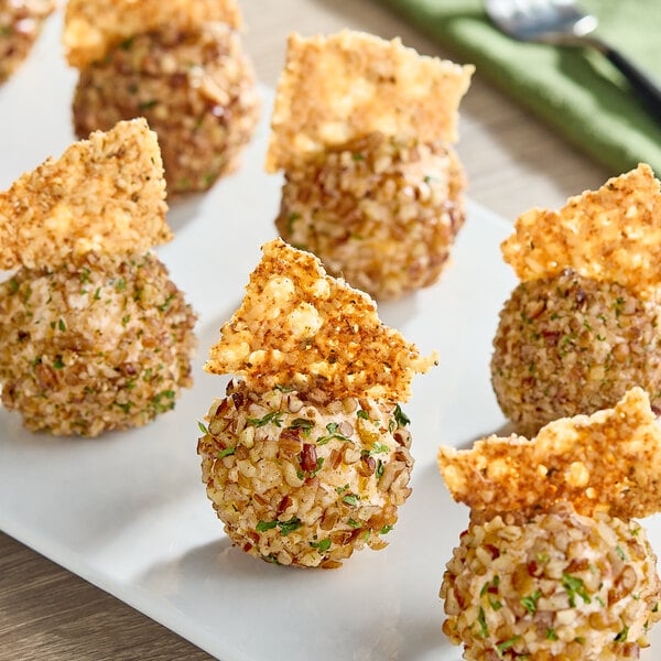 A plate of round cheese balls coated in chopped nuts and herbs, each garnished with a crisp cracker piece.