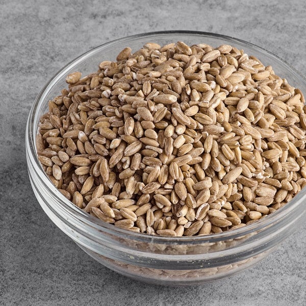 A clear glass bowl filled with organic farro grains on a gray surface.