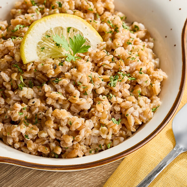 A bowl of cooked organic farro garnished with herbs and a lemon slice.