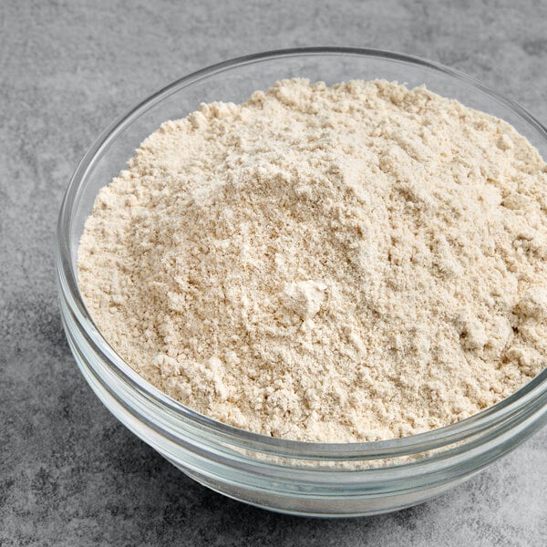 A glass bowl filled with whole wheat flour on a gray surface.