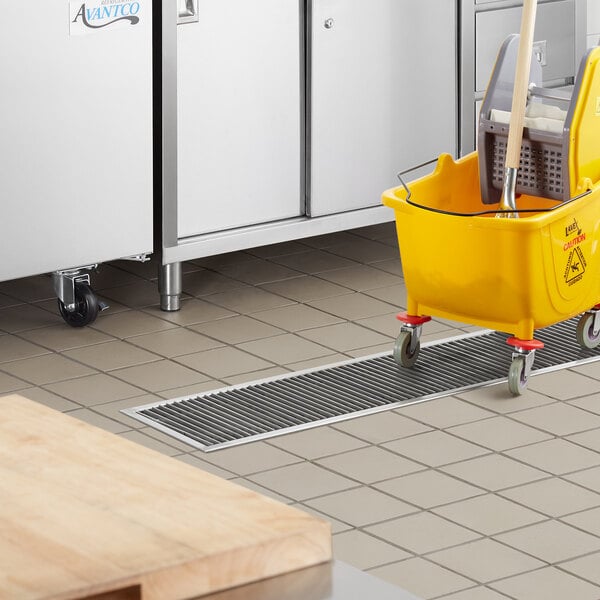 A yellow mop and bucket inside a Regency stainless steel floor trough in a kitchen.