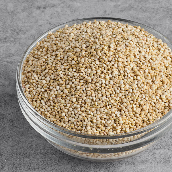 A glass bowl filled with organic white quinoa on a gray surface.