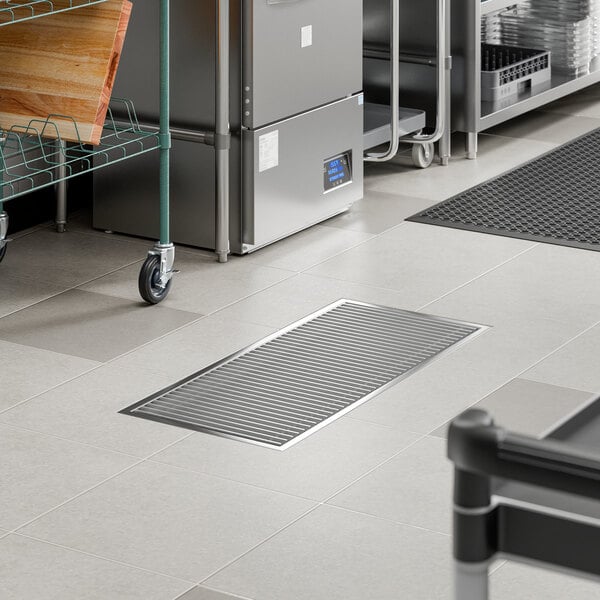 A stainless steel floor trough with a grate, measuring 18 by 42 inches, installed in a commercial kitchen setting.