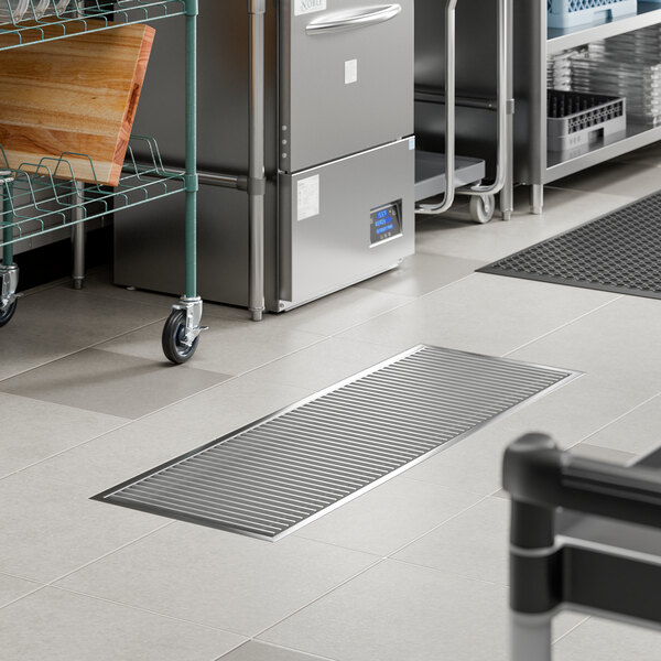 An 18 inch by 54 inch stainless steel floor trough with a grate, installed in a commercial kitchen floor.