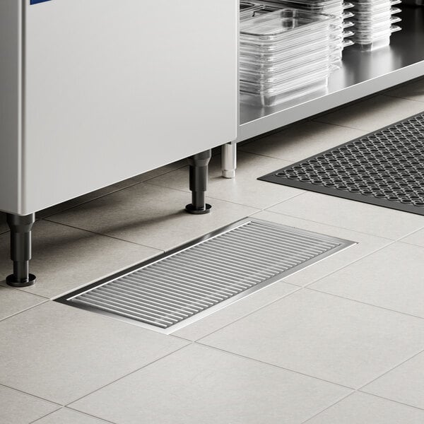 A 12-inch by 30-inch stainless steel floor trough with a grate, installed in a tiled floor.