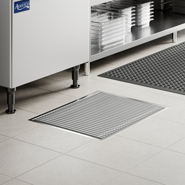 A rectangular stainless steel floor trough with a grate, installed in a tiled floor.