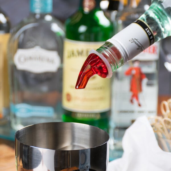 A Tablecraft red liquor pourer dispensing alcohol into a glass.