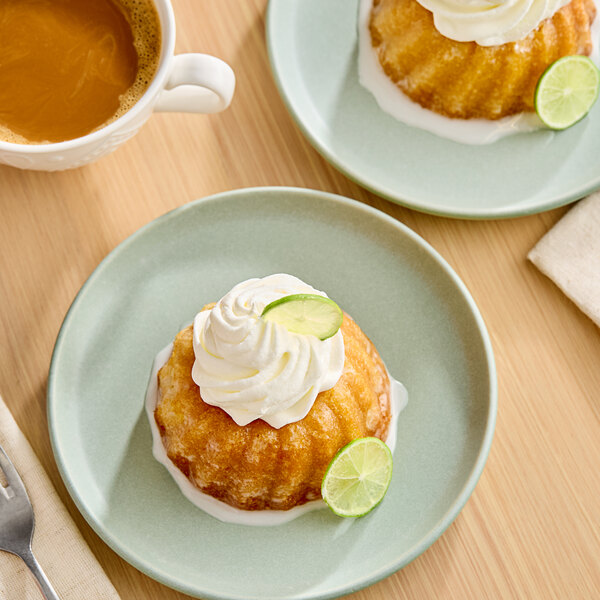 A small bundt cake topped with whipped cream and a lime slice, served on a light green plate with a cup of coffee nearby.