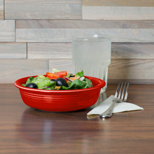 A Fiesta medium scarlet china bowl filled with salad on a table with a water glass and a fork.