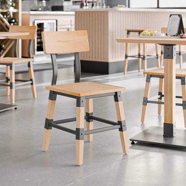 A Lancaster Table & Seating wooden chair with metal accents at a wooden table in a restaurant.