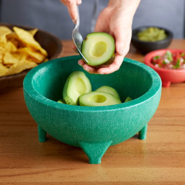 avocados being scooped and added to a molcajete