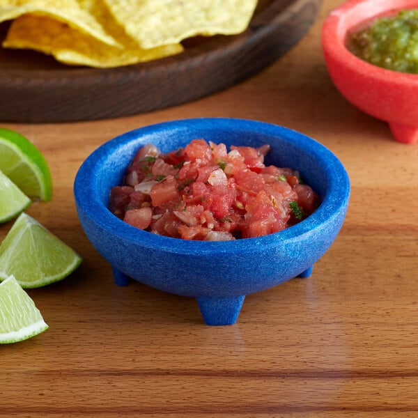 A blue Choice Thermal Plastic Molcajete bowl of salsa and limes on a table.