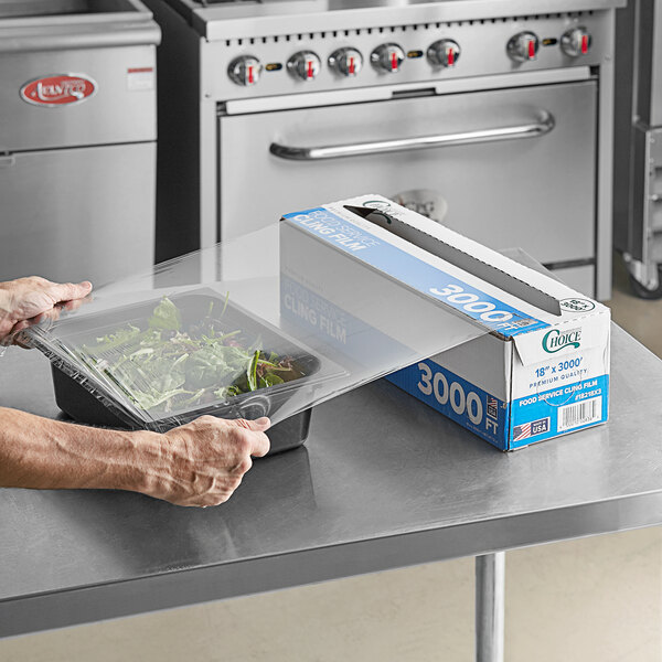A person using Choice Foodservice Film to cover a plastic container of salad.
