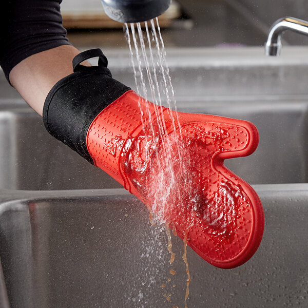 A person washing a red SafeMitt oven mitt.