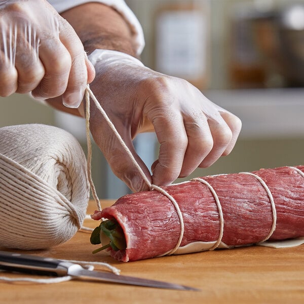 Gloved hands tying butcher twine around meat with herbs