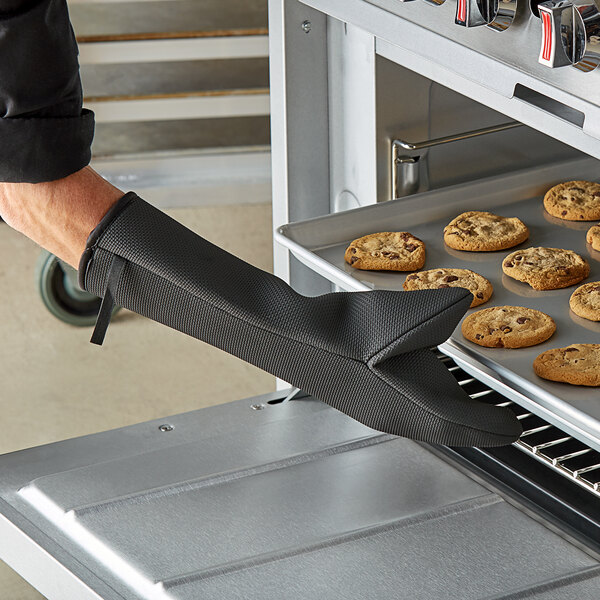 A person wearing a SafeMitt oven mitt and glove taking cookies out of the oven.