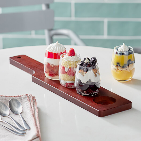 An Acopa mahogany tasting flight paddle with stemless wine glasses filled with fruit desserts on a wooden board.