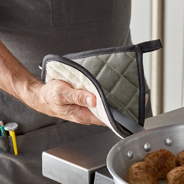 A person using a Choice flame retardant terry cloth pot holder to hold a cooking pot of meatballs.