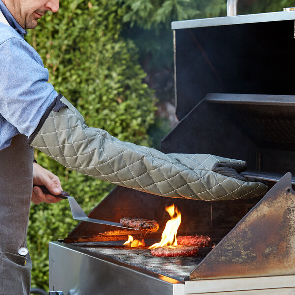 A man using a SafeMitt puppet style oven mitt to cook burgers on a grill.