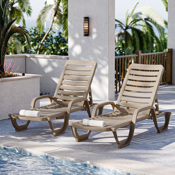 Two Grosfillex taupe resin chaise lounges on a patio.