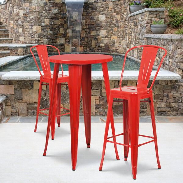 A red metal bar height table with two red bar stools on an outdoor patio.