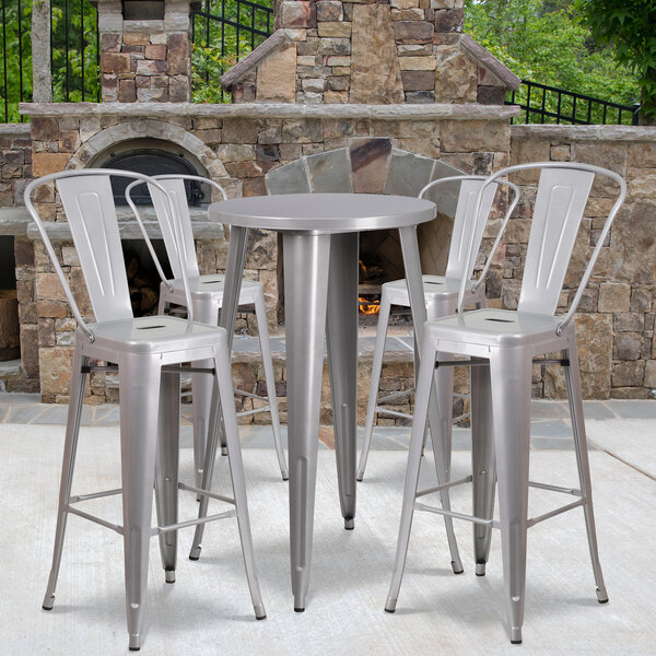 A Flash Furniture silver metal bar height table with four silver metal stools on an outdoor patio.