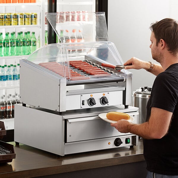 A man using an Avantco slanted hot dog roller to cook hot dogs.