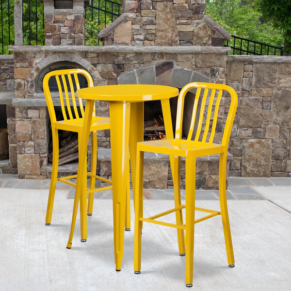 A yellow table with a black band and two yellow stools in front of a stone fireplace.