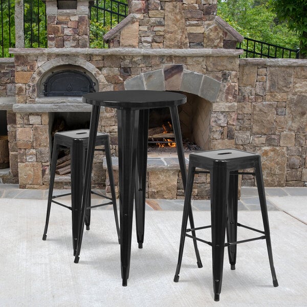 A Flash Furniture black metal bar height table with two square black stools on a stone patio.