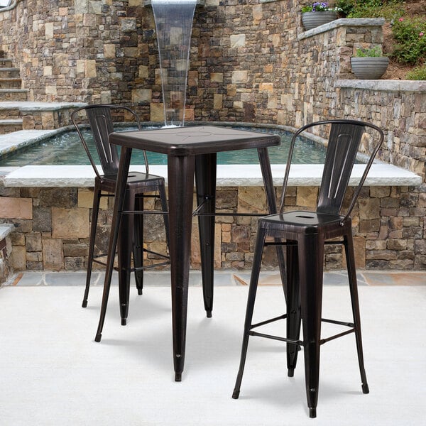 A Flash Furniture black metal square bar height table with two chairs on an outdoor patio next to a water fountain.