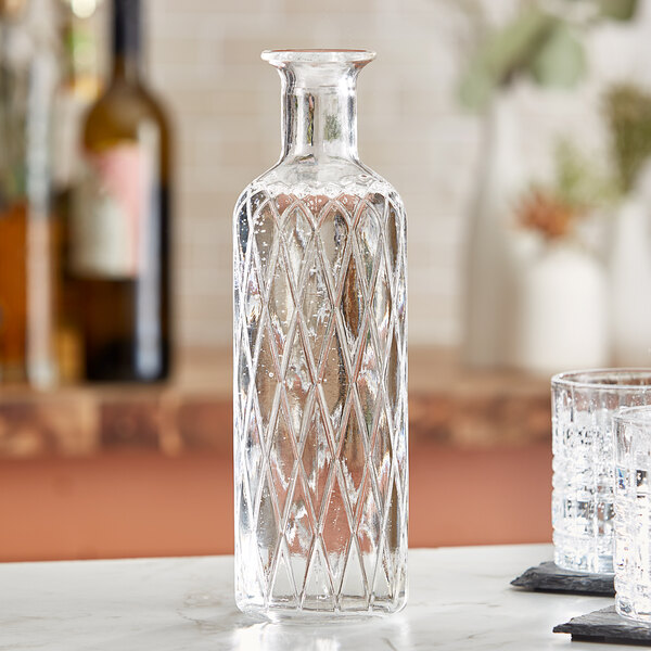 An American Metalcraft clear glass carafe with a diamond pattern on a table.