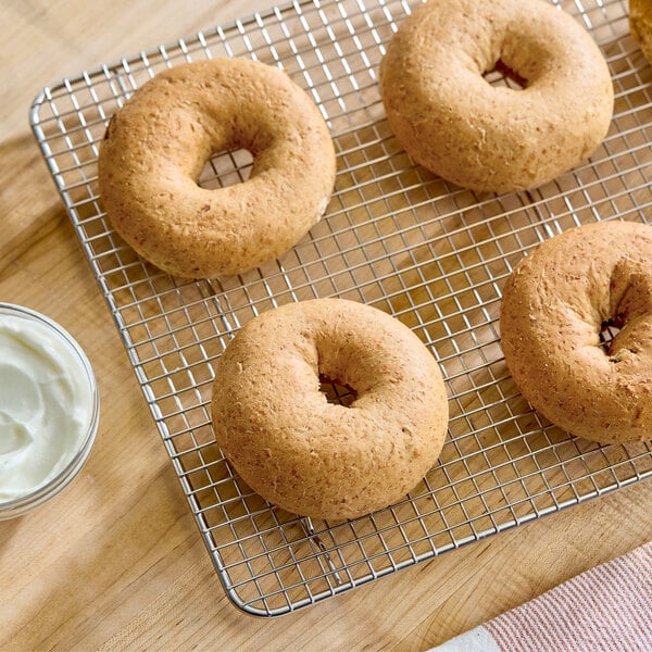 A batch of whole wheat bagels cooling on a wire rack next to a small bowl of cream cheese.