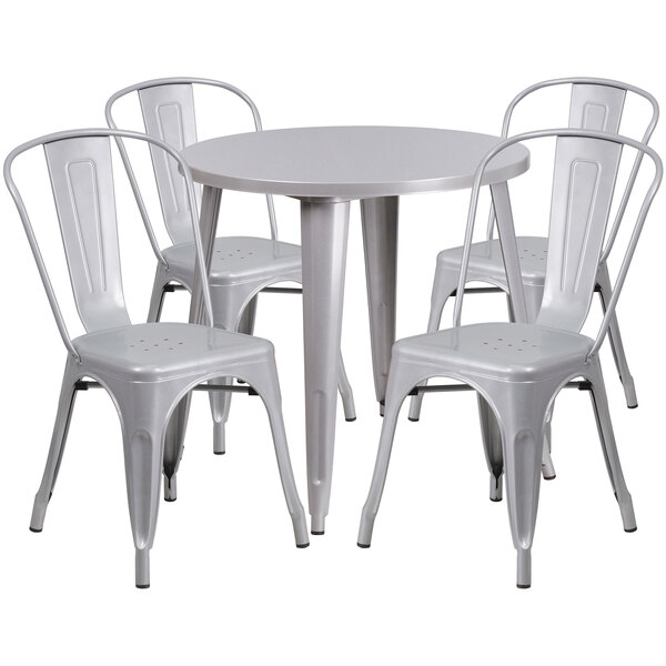 A round silver metal table with white chairs around it.