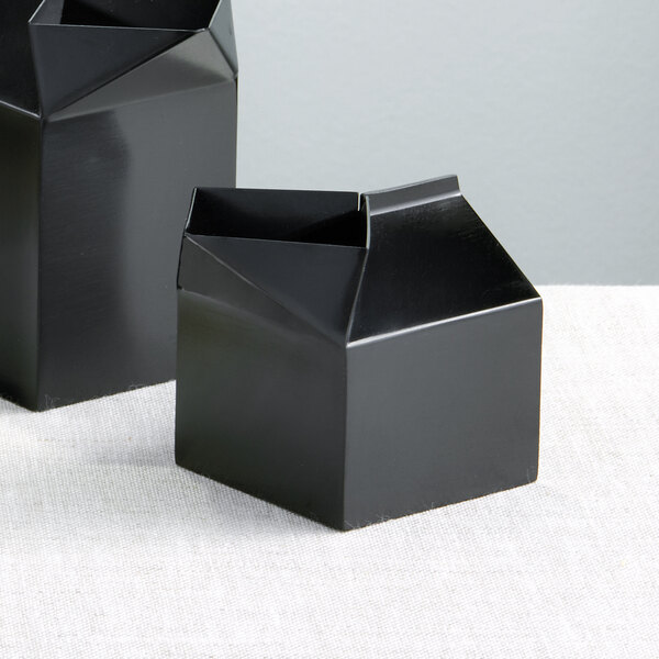 Two black American Metalcraft milk carton creamers on a table.