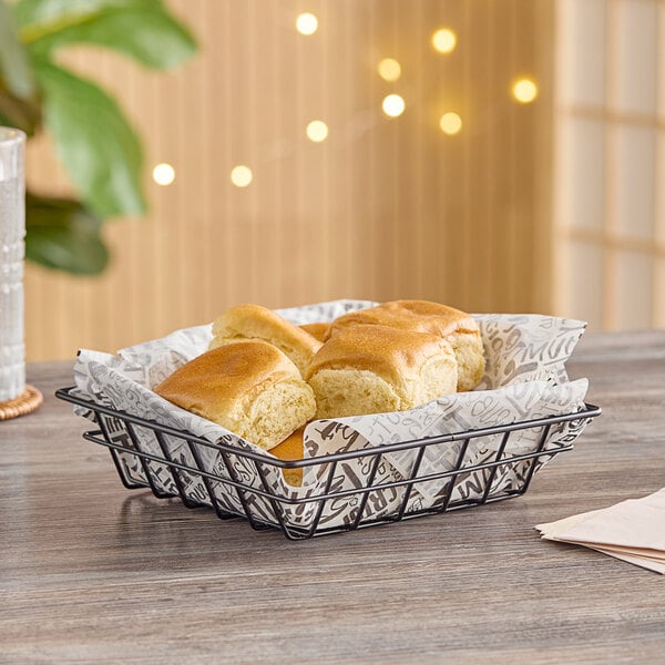 A black square wire basket filled with rolls on a table.