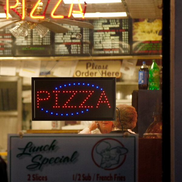 A rectangular LED pizza sign with lights on a counter in a pizza parlor.