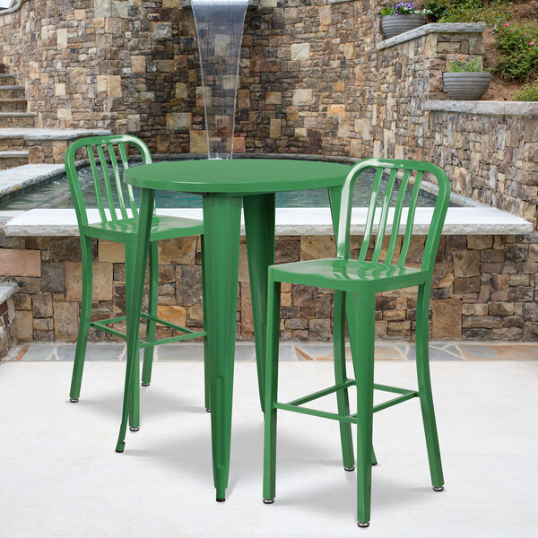 A green Flash Furniture bar table with two green chairs on an outdoor patio in front of a stone wall.