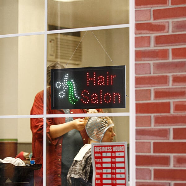 A woman getting her hair done in a hair salon under a lighted rectangular LED sign.