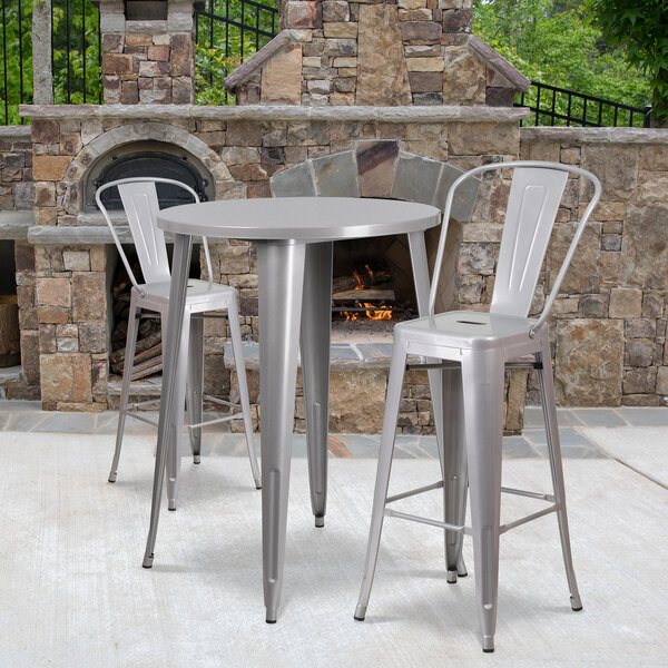 A Flash Furniture metal bar height table and two chairs on an outdoor patio with a fireplace.
