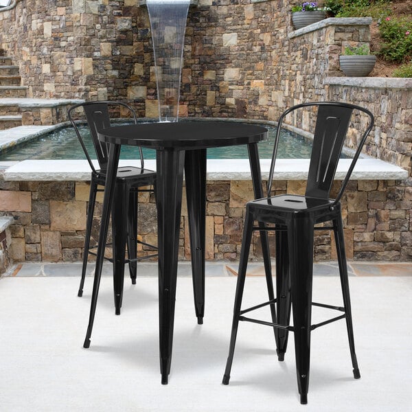 A Flash Furniture black metal bar height table with 2 black bar stools on a stone patio.