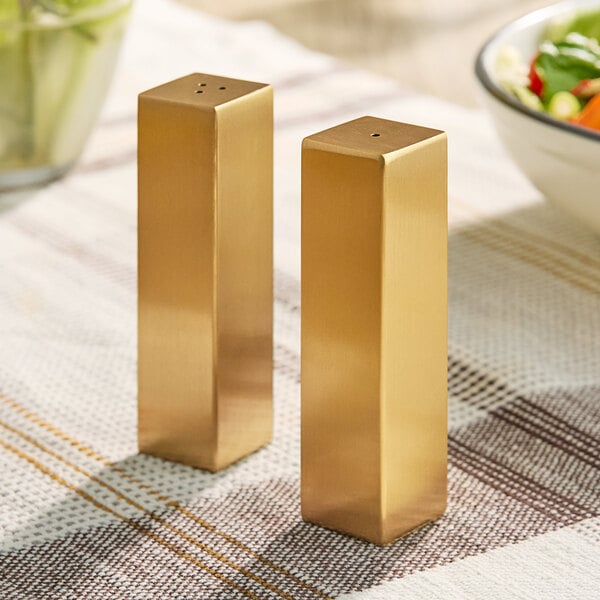 Two gold rectangular salt and pepper shakers on a table.