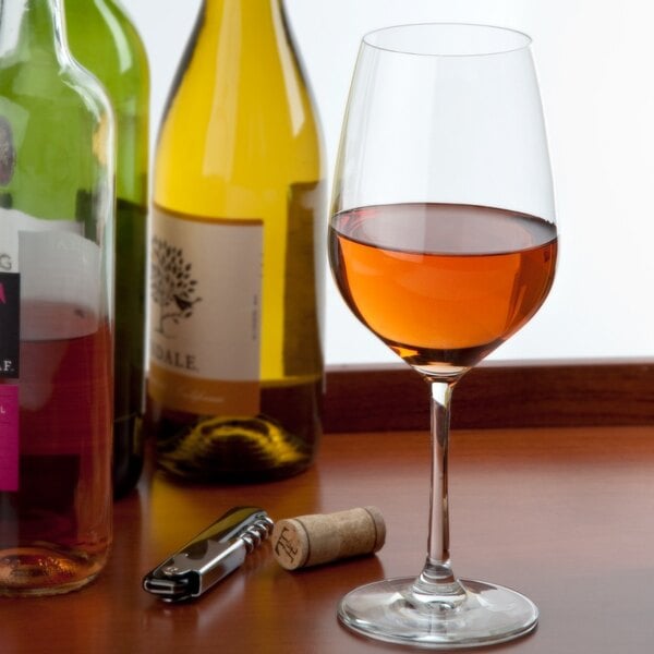 A Stolzle Grand Cuvée Bordeaux wine glass filled with wine next to bottles of wine.