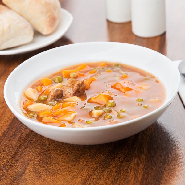 An Arcoroc white soup bowl filled with soup on a table.