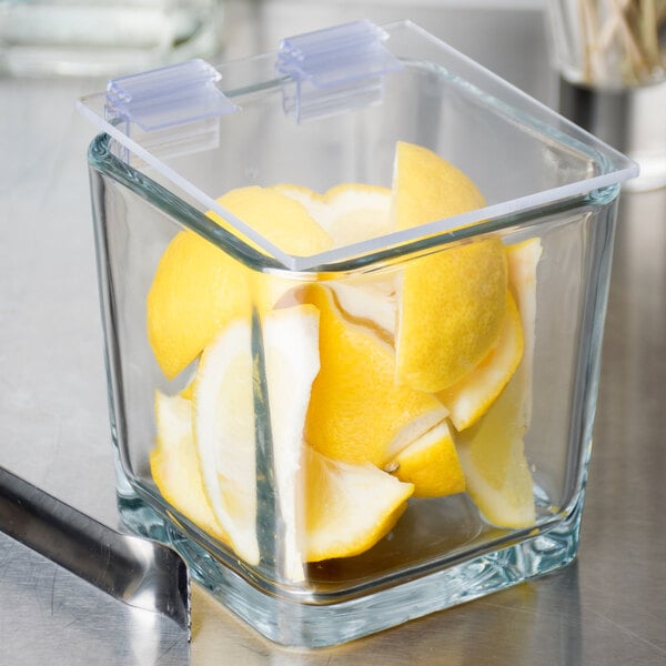 A Cal-Mil hinged hard plastic lid on a glass container with lemons inside.