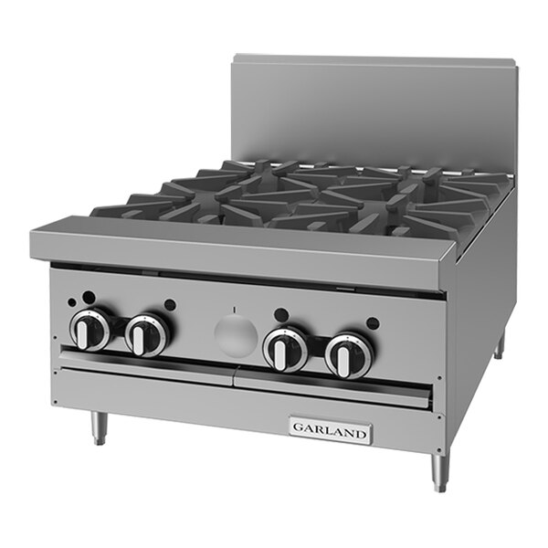 A stainless steel 4-burner commercial gas range top with control knobs and a backsplash.