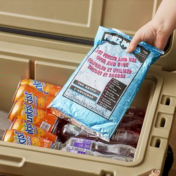 A hand holding a Lifoam Freez Pak reusable ice pack bag of frozen water and soda cans.