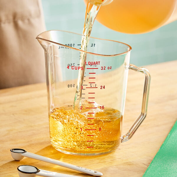 A close up of a person pouring liquid into a Cambro clear polycarbonate measuring cup.