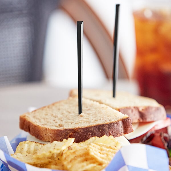 A sandwich with chips and a Royal Paper black plastic prism food pick on a plate.